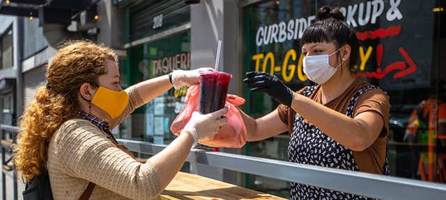 Photo of a restaurant worker handing customer takeout in masks