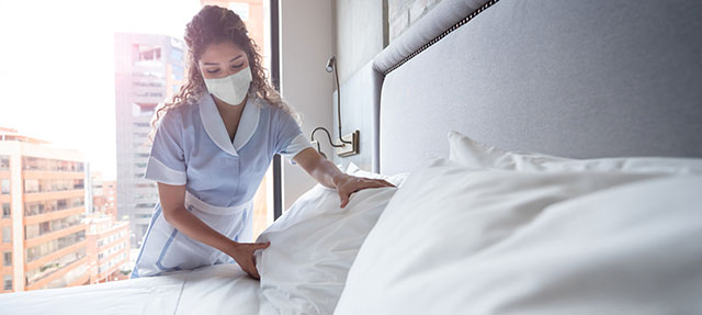 photo - Hotel Maid Making Bed and Wearing Mask
