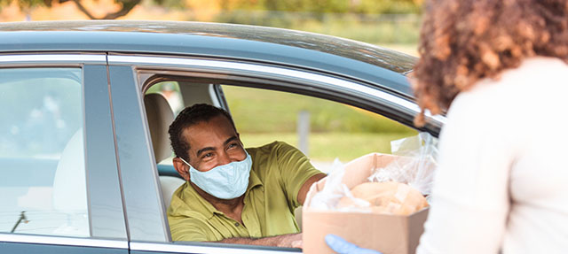 photo - Man in Car Wearing Mask and Picking Up Box of Food