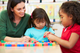 photo - Teacher Working with Two Students at Table with Counting Blocks