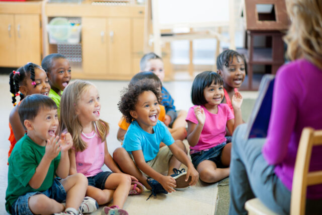 photo - Preschool Students Sitting on Rug and Listening to Teacher Reading a Book