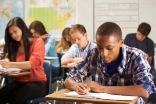 photo - Students at Desks in Classroom Writing in Notebooks