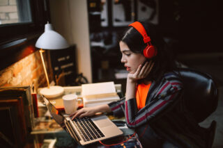 photo - Young Woman at Home Wearing Headphones on Laptop