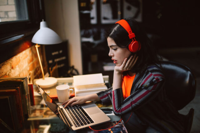 photo - Young Woman at Home Wearing Headphones on Laptop