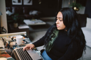 photo - Young Woman Sitting at Desk in her Los Angeles Apartment, Typing on a Laptop