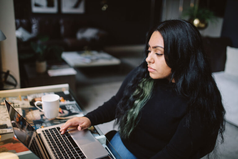 photo - Young Woman Sitting at Desk in her Los Angeles Apartment, Typing on a Laptop